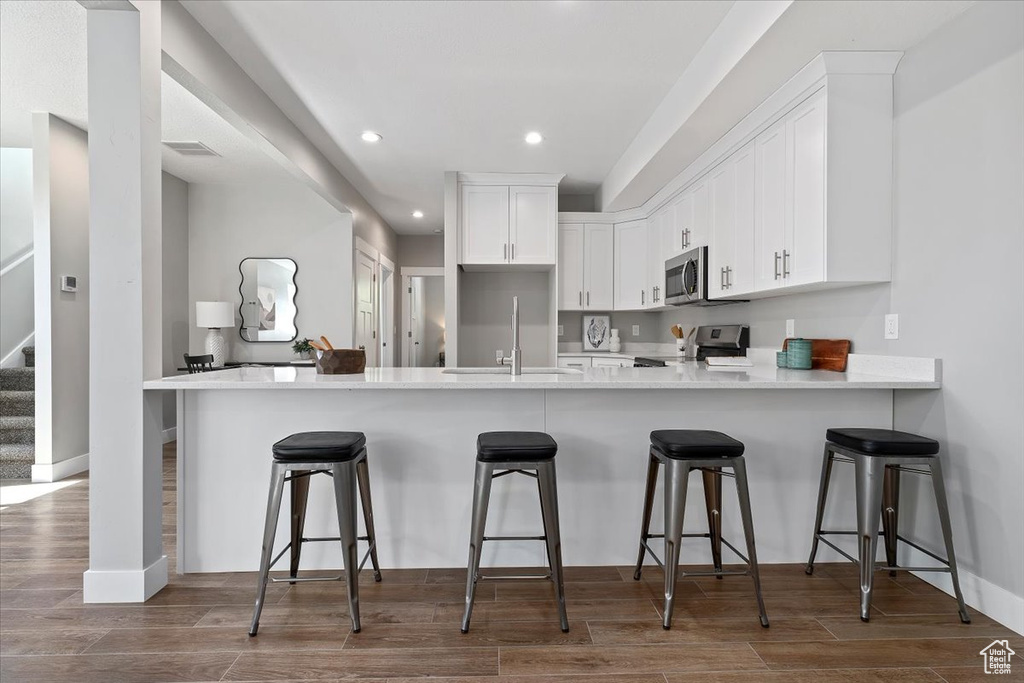 Kitchen with appliances with stainless steel finishes, a sink, a peninsula, recessed lighting, and white cabinetry
