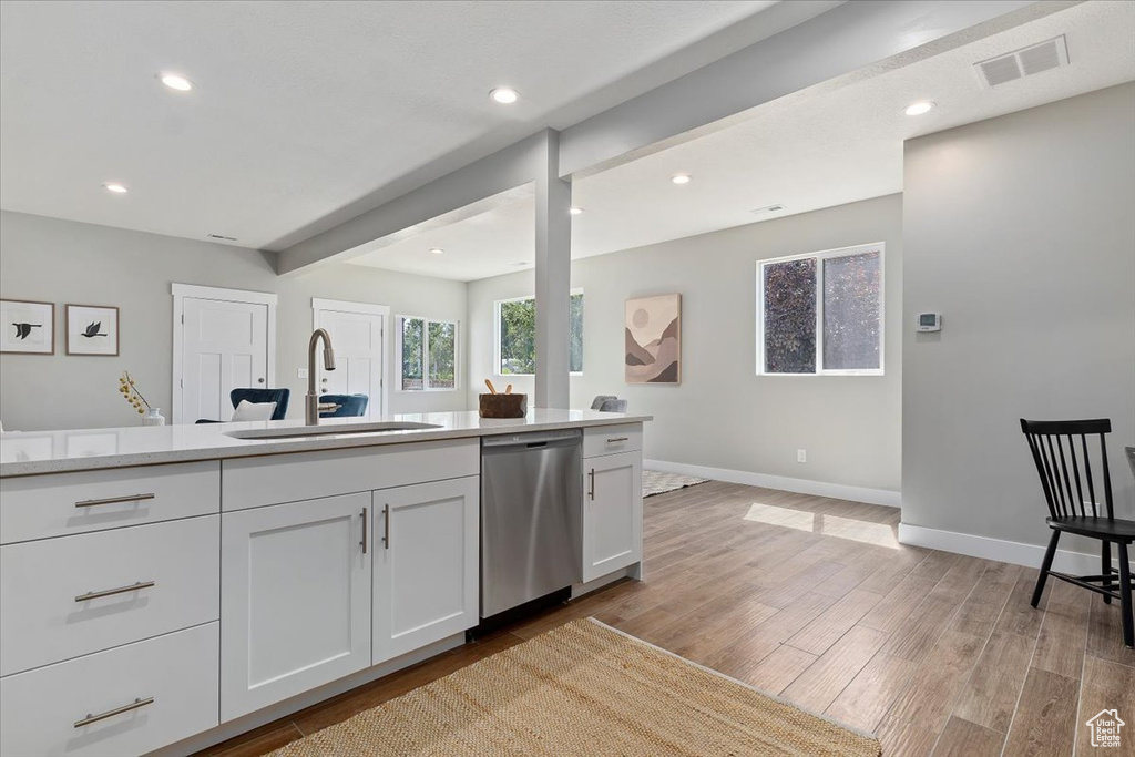 Kitchen featuring visible vents, stainless steel dishwasher, light wood-type flooring, a sink, and white cabinets