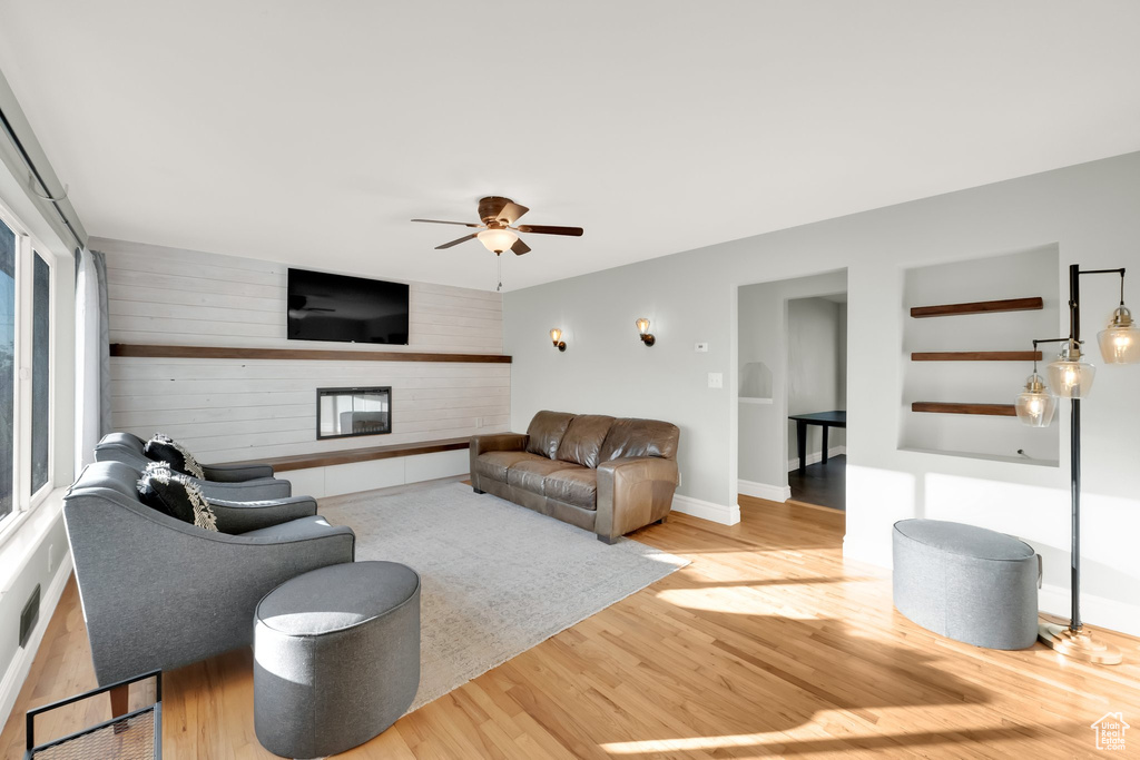 Living room with wooden walls, ceiling fan, a large fireplace, baseboards, and wood finished floors