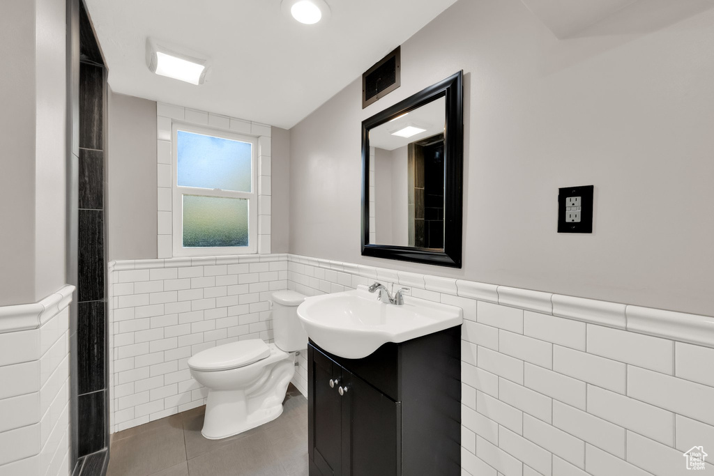Bathroom featuring vanity, toilet, tile walls, and a wainscoted wall
