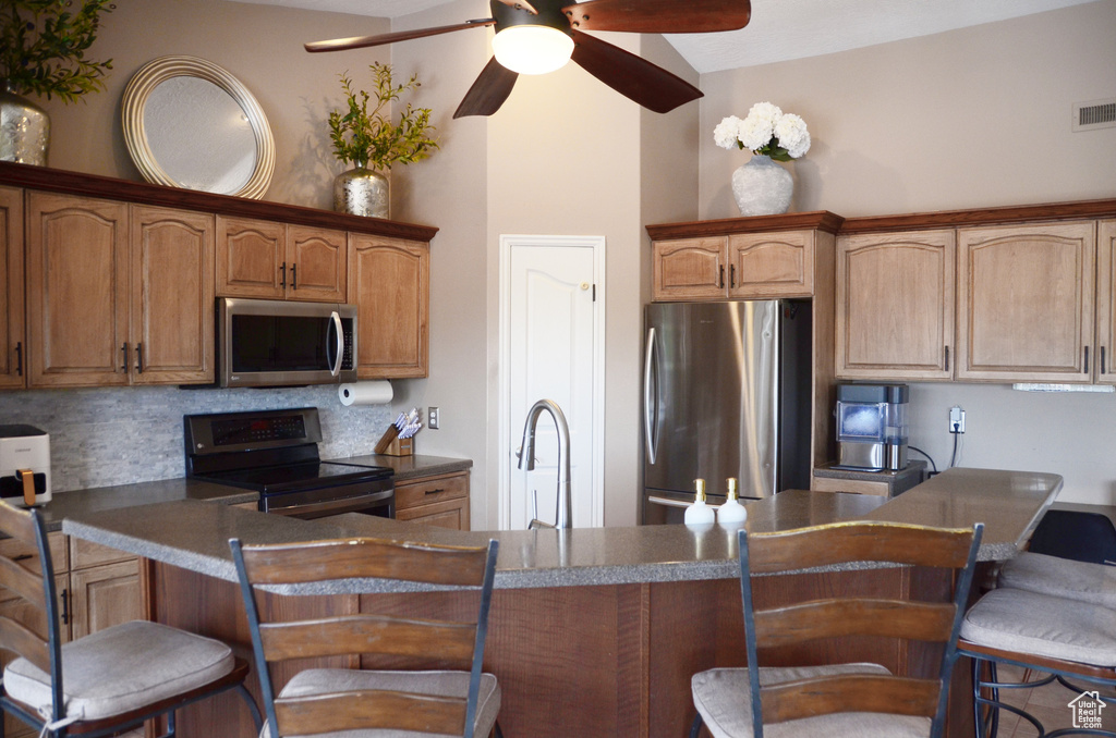 Kitchen featuring a kitchen breakfast bar, a ceiling fan, backsplash, appliances with stainless steel finishes, and a sink