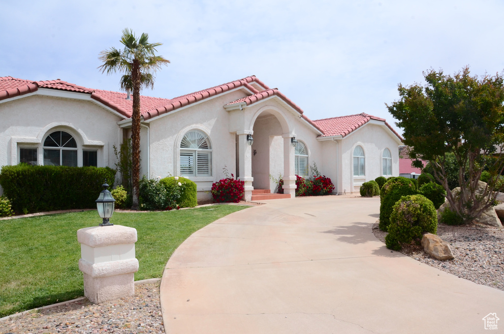 Mediterranean / spanish-style home with stucco siding, concrete driveway, a tile roof, and a front lawn