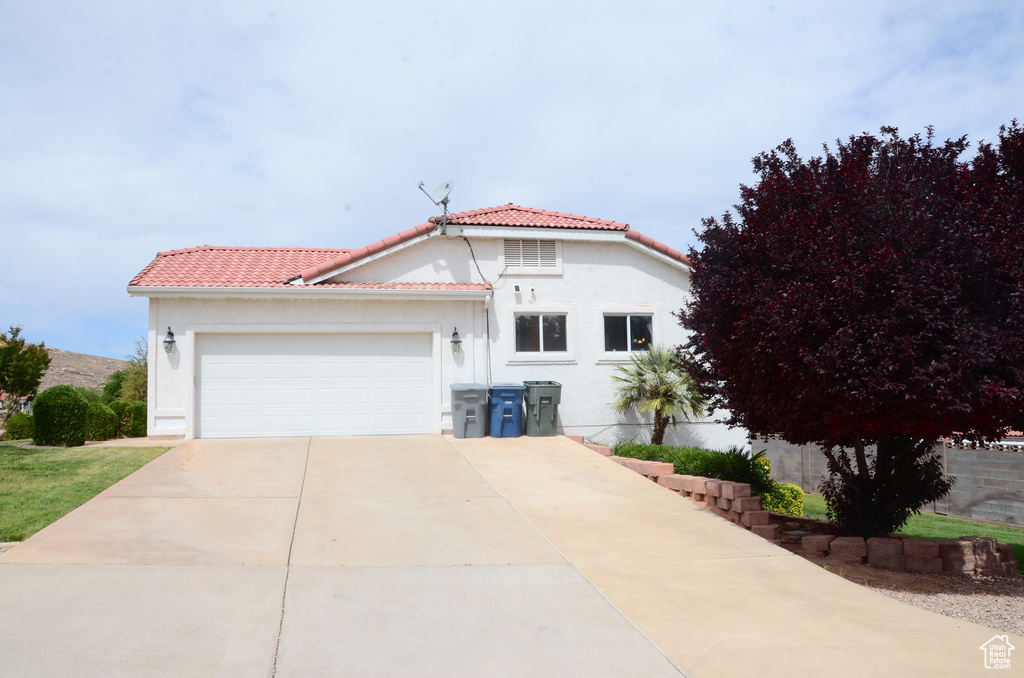 Mediterranean / spanish-style home featuring a garage, stucco siding, a tiled roof, and driveway