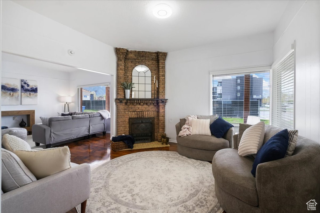 Living area with a brick fireplace, dark wood finished floors, and a healthy amount of sunlight