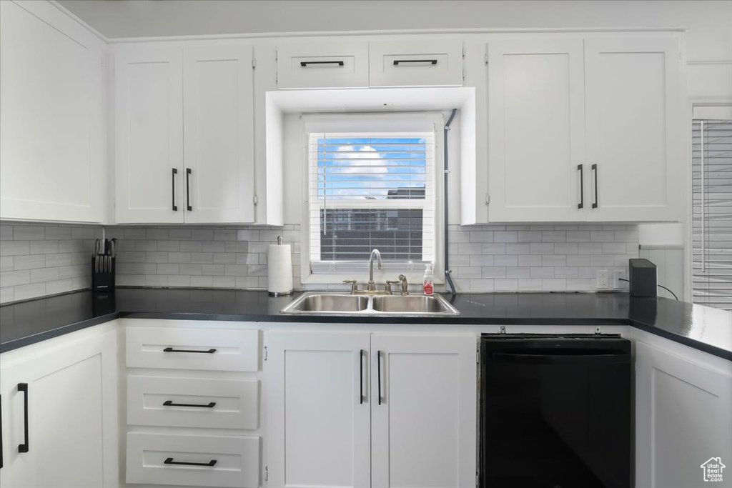 Kitchen featuring a sink, backsplash, dark countertops, dishwasher, and white cabinets