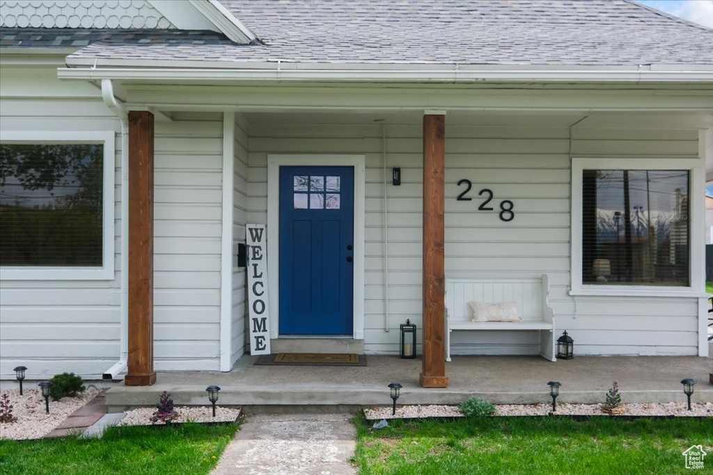 Doorway to property with a porch and a shingled roof