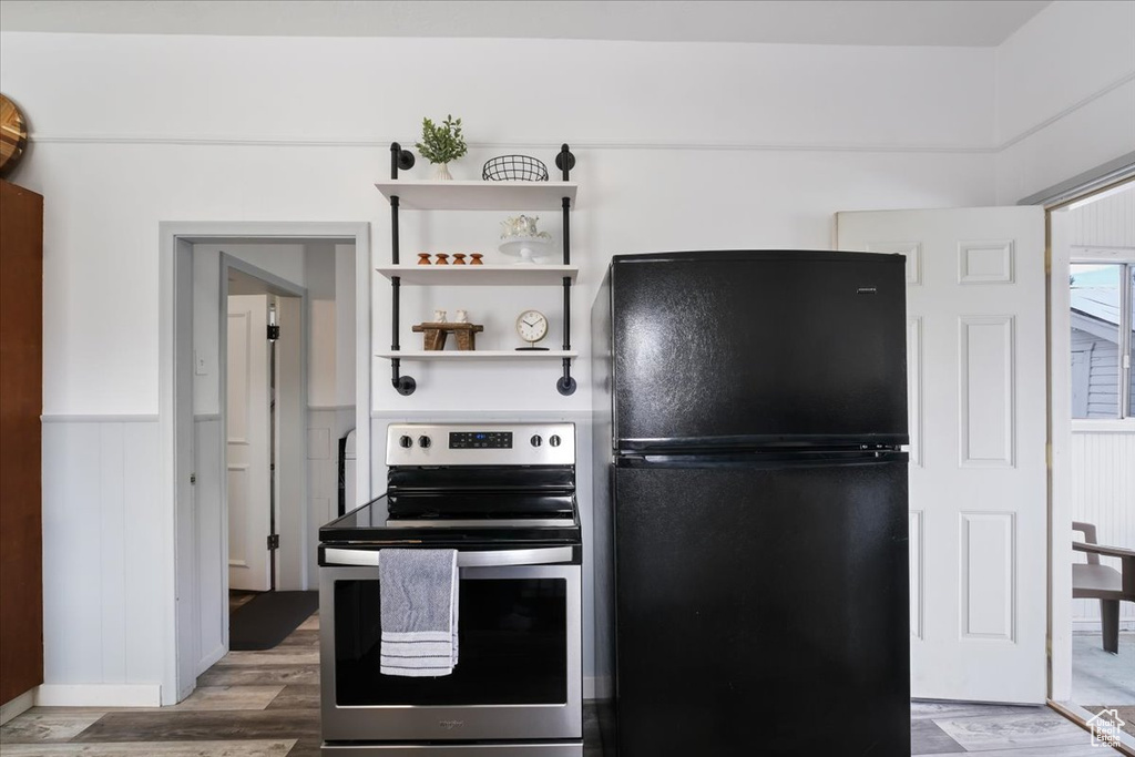 Kitchen with wood finished floors, stainless steel range with electric cooktop, freestanding refrigerator, and wainscoting