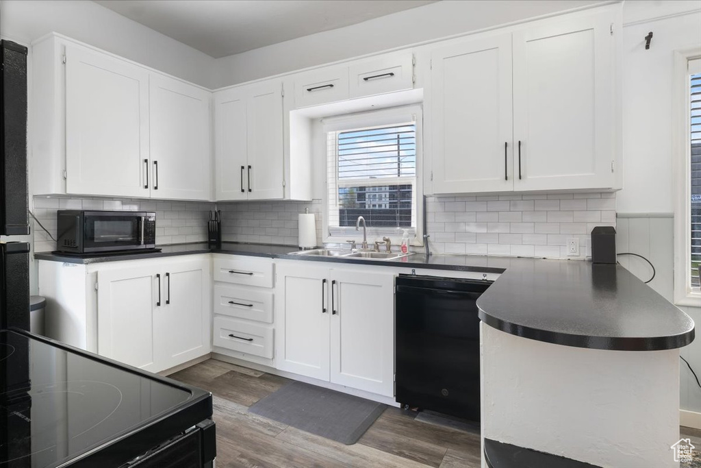 Kitchen with white cabinetry, a sink, dark countertops, dishwasher, and wood finished floors
