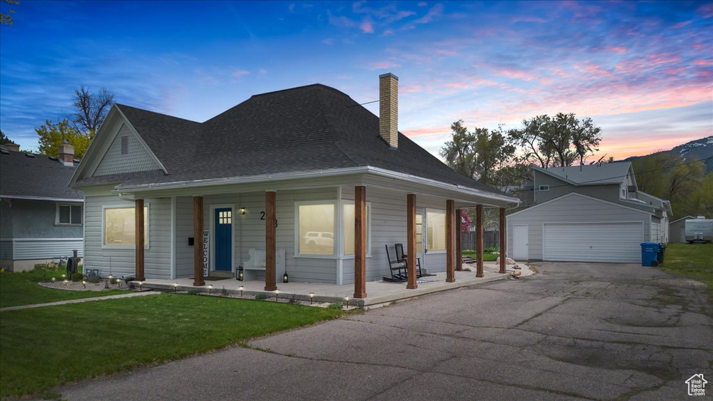 Farmhouse-style home featuring a chimney, an outbuilding, a porch, a front lawn, and a garage
