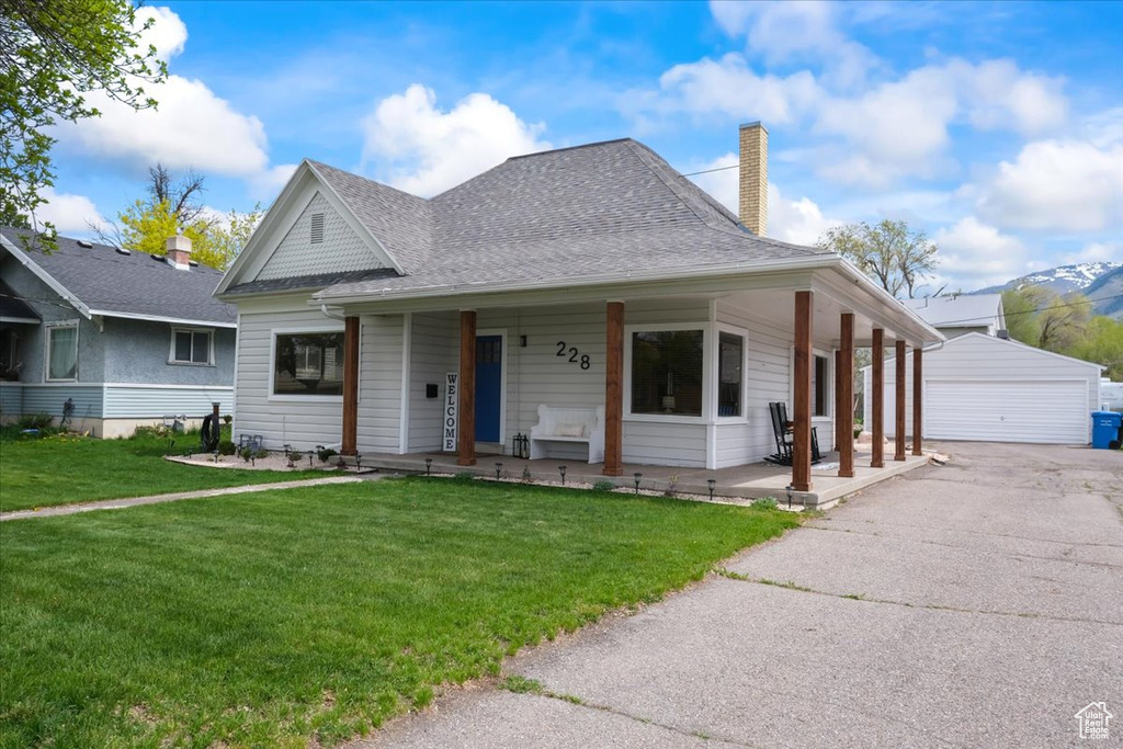Country-style home featuring a chimney, an outdoor structure, covered porch, a detached garage, and a front yard