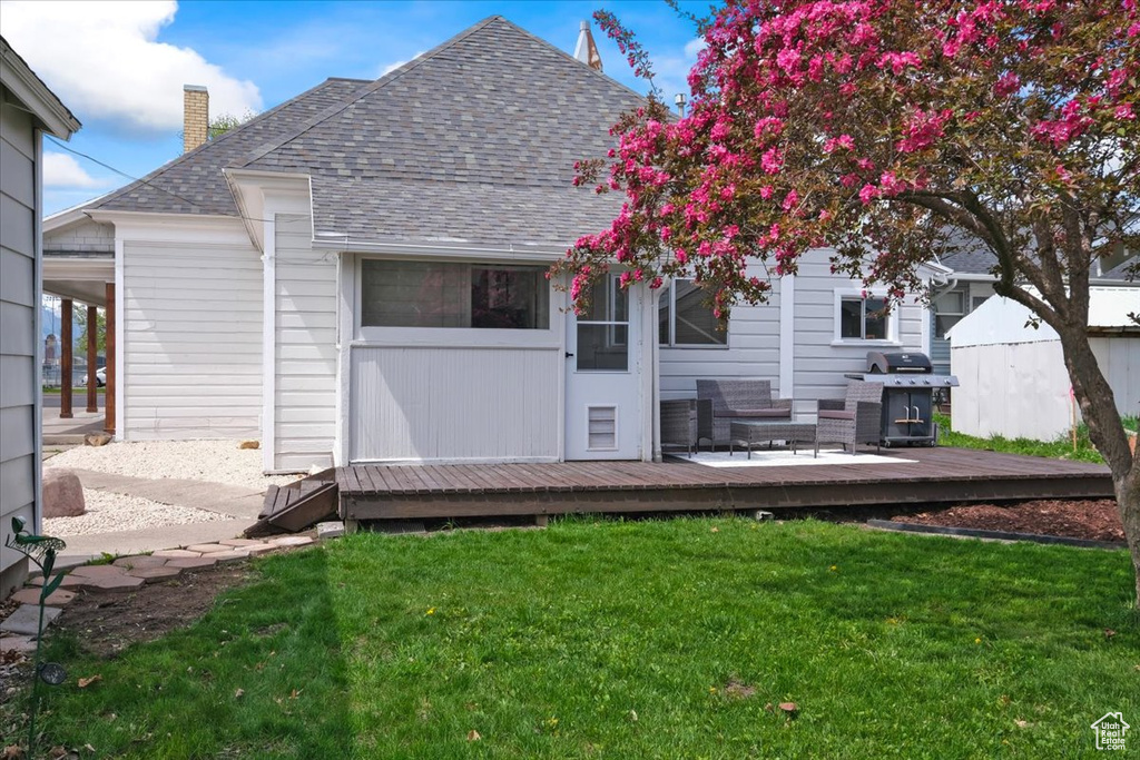 Rear view of property featuring a lawn, a deck, a chimney, and roof with shingles