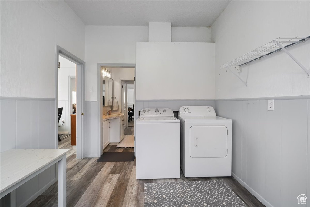Clothes washing area featuring a sink, laundry area, a wainscoted wall, washer and dryer, and dark wood finished floors