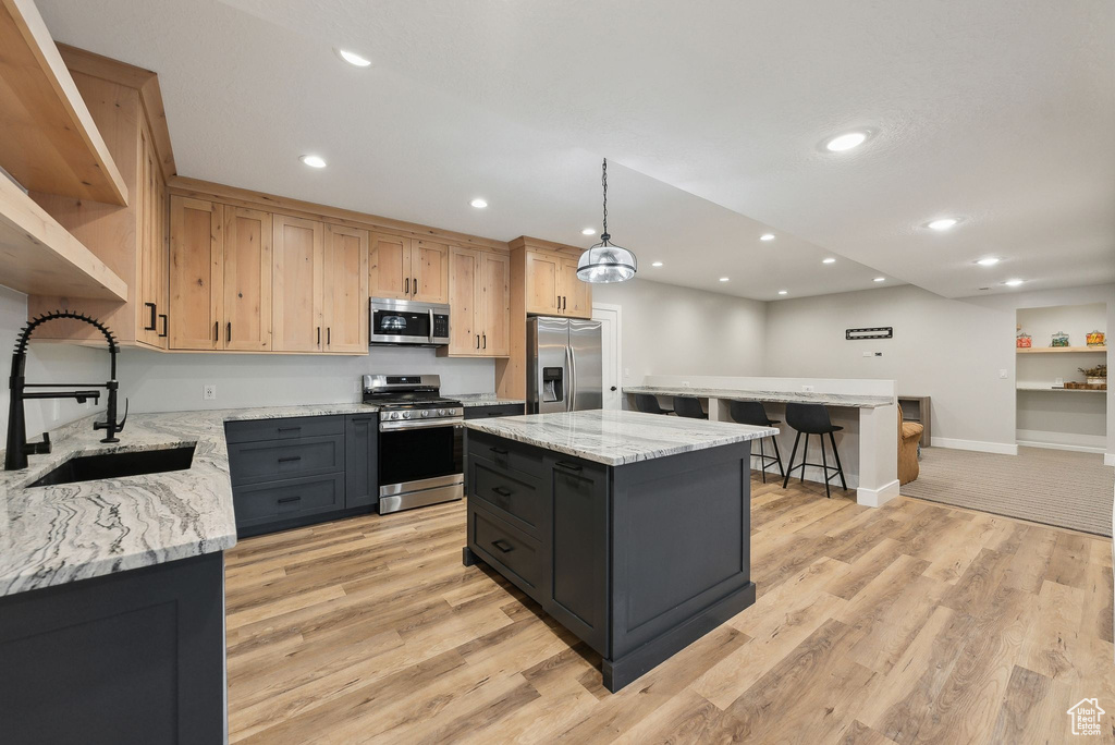 Kitchen with a kitchen island, a kitchen bar, a sink, light wood-style flooring, and stainless steel appliances