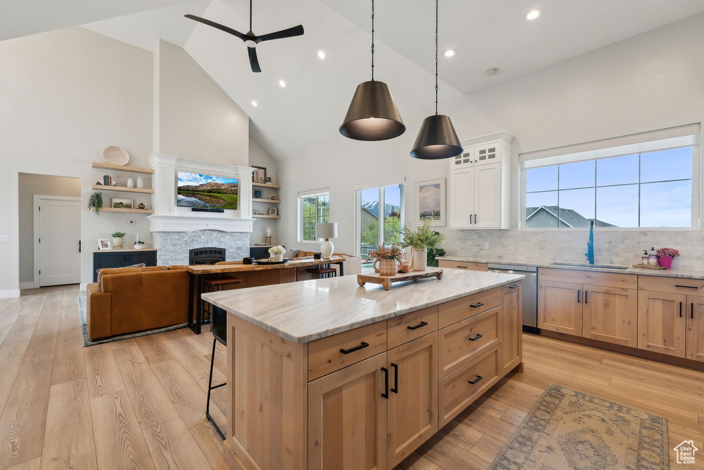 Kitchen featuring high vaulted ceiling, a stone fireplace, a center island, a ceiling fan, and stainless steel dishwasher