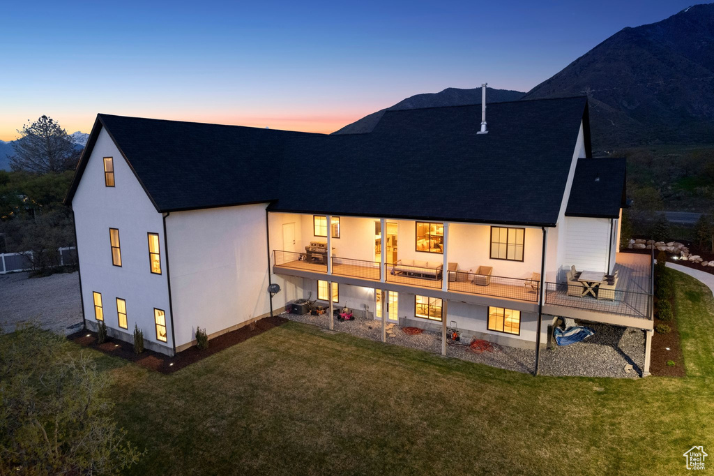 Back of house at dusk with a balcony, stucco siding, a yard, and roof with shingles
