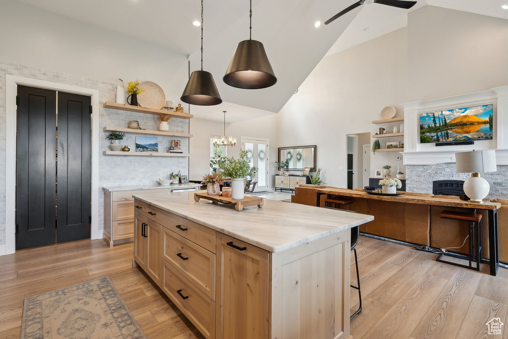 Kitchen featuring open shelves, pendant lighting, high vaulted ceiling, light wood-type flooring, and light stone counters