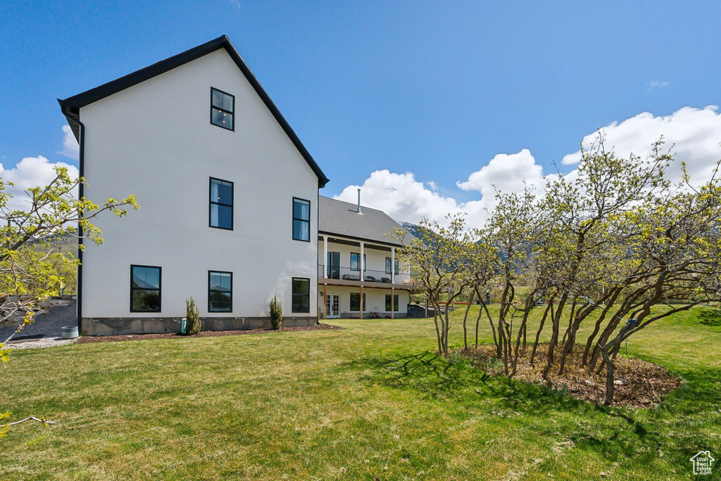Rear view of property with a lawn, stucco siding, and a balcony