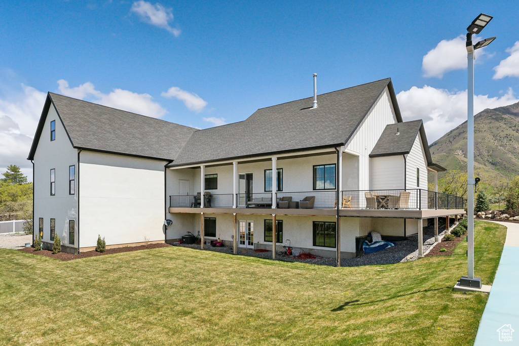 Rear view of property featuring a lawn, a mountain view, roof with shingles, and a balcony
