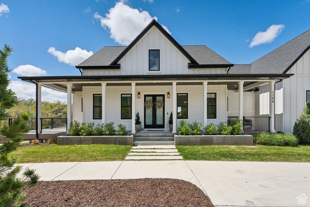Modern farmhouse style home featuring a porch, board and batten siding, french doors, and a front yard