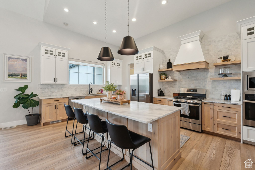 Kitchen featuring appliances with stainless steel finishes, a center island, open shelves, a sink, and custom exhaust hood