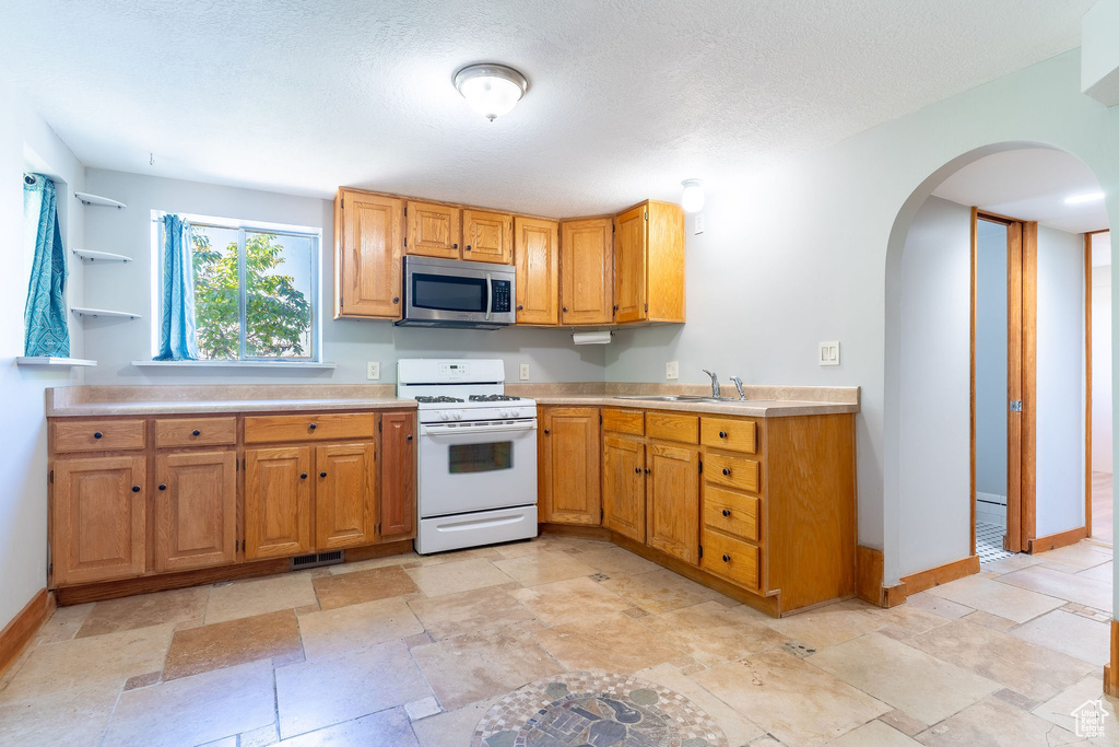 Kitchen with white gas stove, a sink, stainless steel microwave, arched walkways, and light countertops