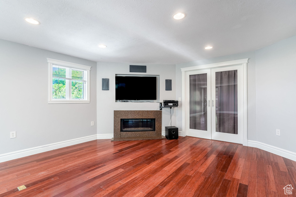 Unfurnished living room with baseboards, french doors, a fireplace with flush hearth, and wood finished floors