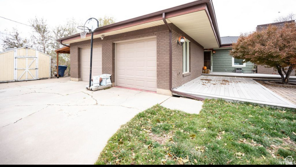 Exterior space with an attached garage, a storage unit, brick siding, and concrete driveway