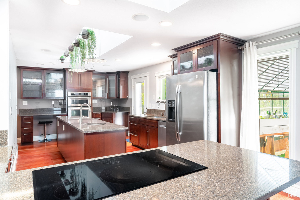 Kitchen with a sink, stainless steel appliances, wood finished floors, and a center island with sink