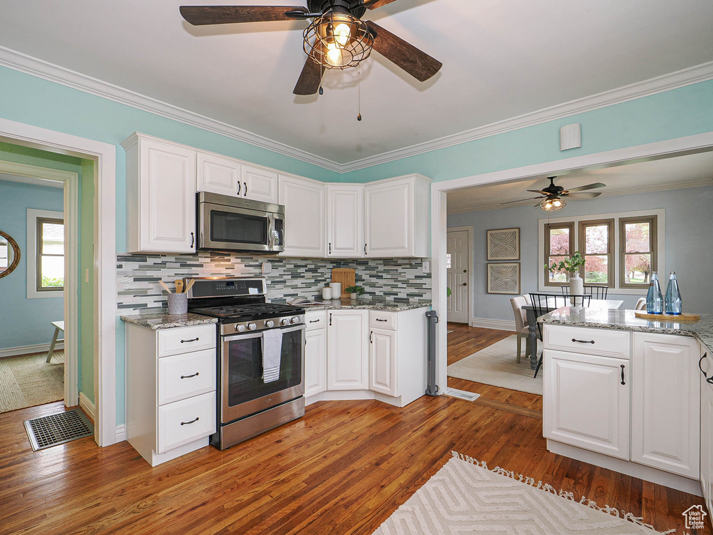 Kitchen with ceiling fan, appliances with stainless steel finishes, white cabinets, light wood-style floors, and ornamental molding