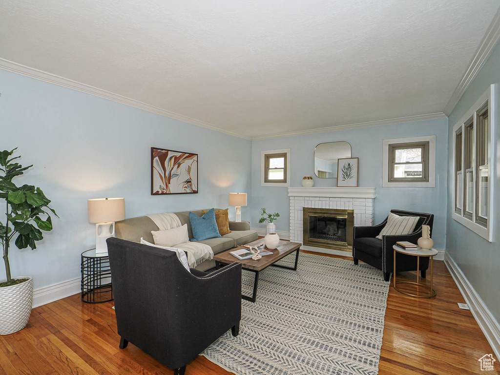 Living area with baseboards, ornamental molding, a brick fireplace, and light wood-style flooring