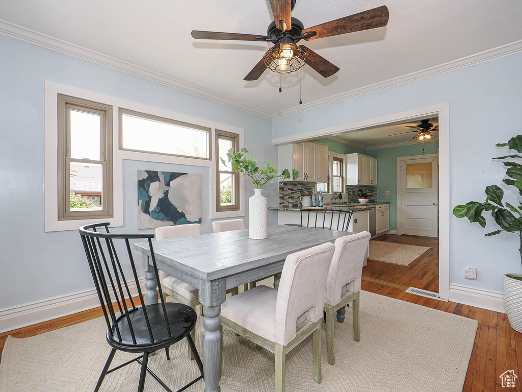 Dining room featuring light wood-style floors, a ceiling fan, baseboards, visible vents, and ornamental molding