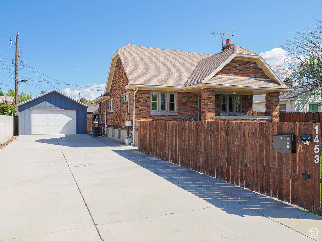 View of side of property featuring a shingled roof, fence, and a detached garage