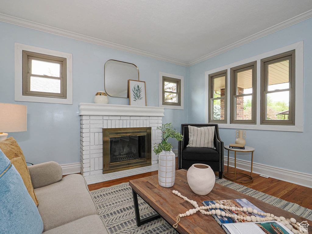 Living room featuring crown molding, baseboards, a brick fireplace, and wood finished floors