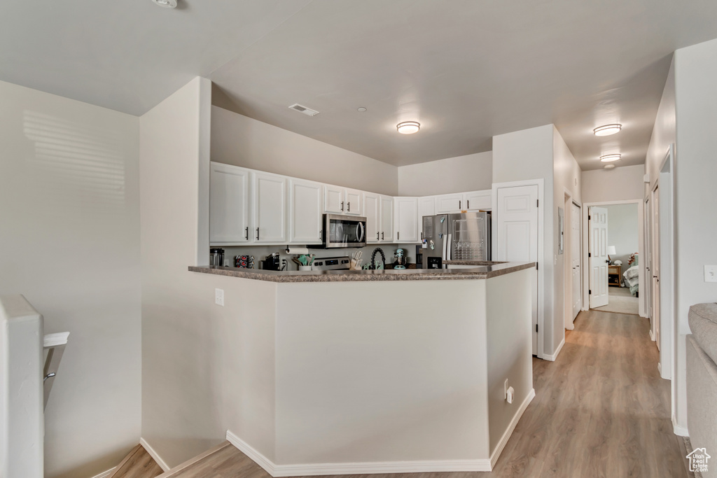 Kitchen featuring light wood-style floors, stainless steel appliances, a peninsula, and white cabinetry