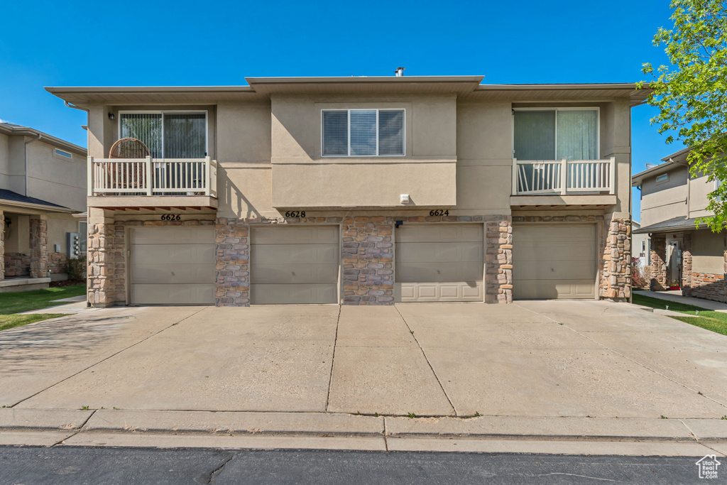 View of front facade featuring an attached garage, driveway, stone siding, and stucco siding