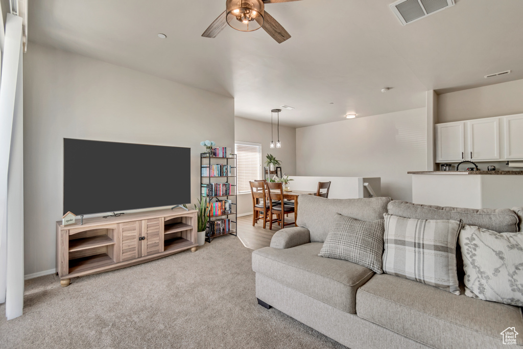 Living area featuring a ceiling fan, visible vents, and light carpet