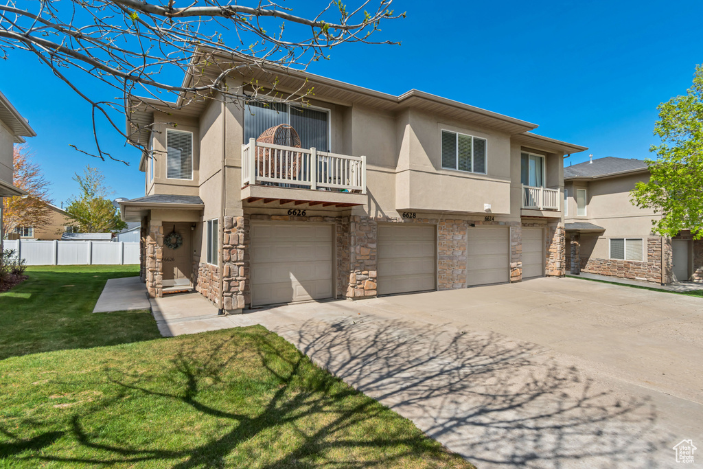 View of front of home with stone siding, a garage, stucco siding, concrete driveway, and a balcony
