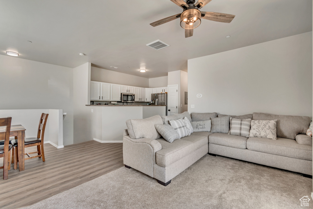Living area with light wood-style floors, baseboards, ceiling fan, and visible vents