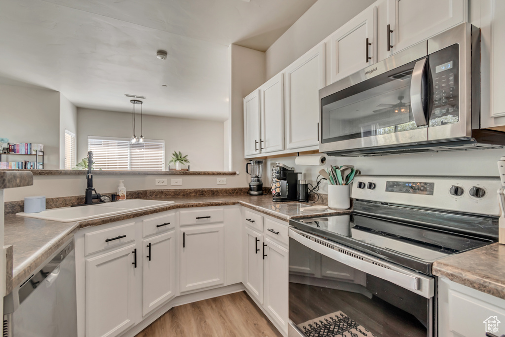 Kitchen with a sink, stainless steel appliances, light wood-style flooring, and white cabinetry