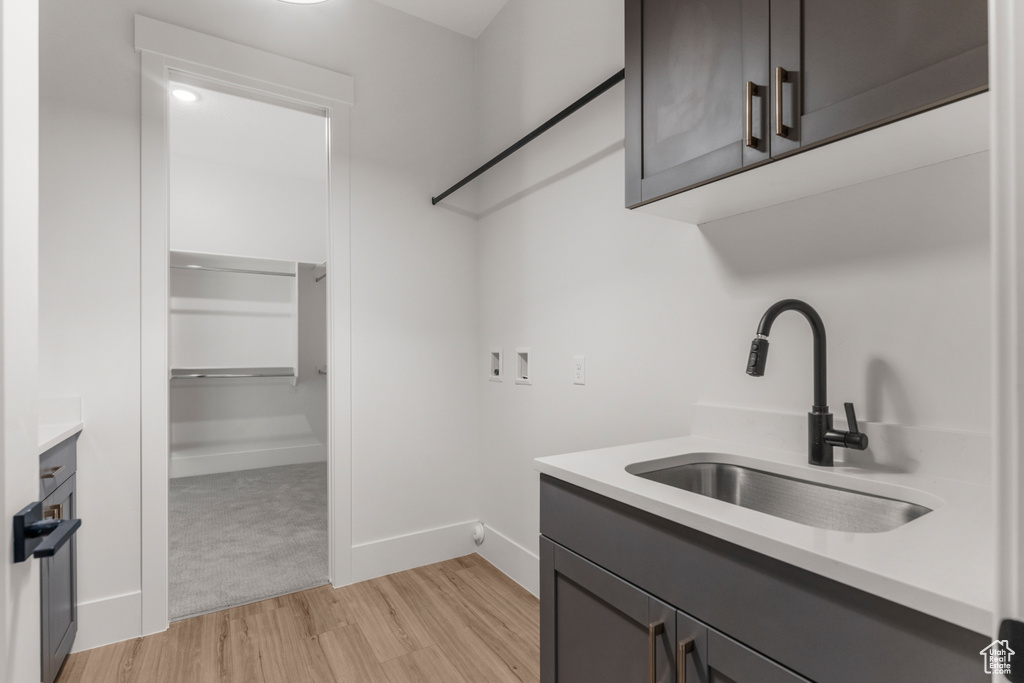 Clothes washing area with cabinet space, a sink, baseboards, hookup for a washing machine, and light wood-style floors