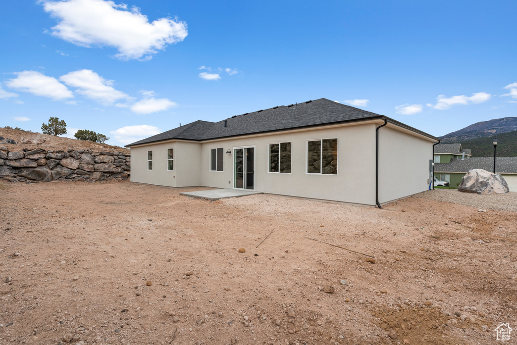 Back of house with a shingled roof, a patio, stucco siding, and a mountain view