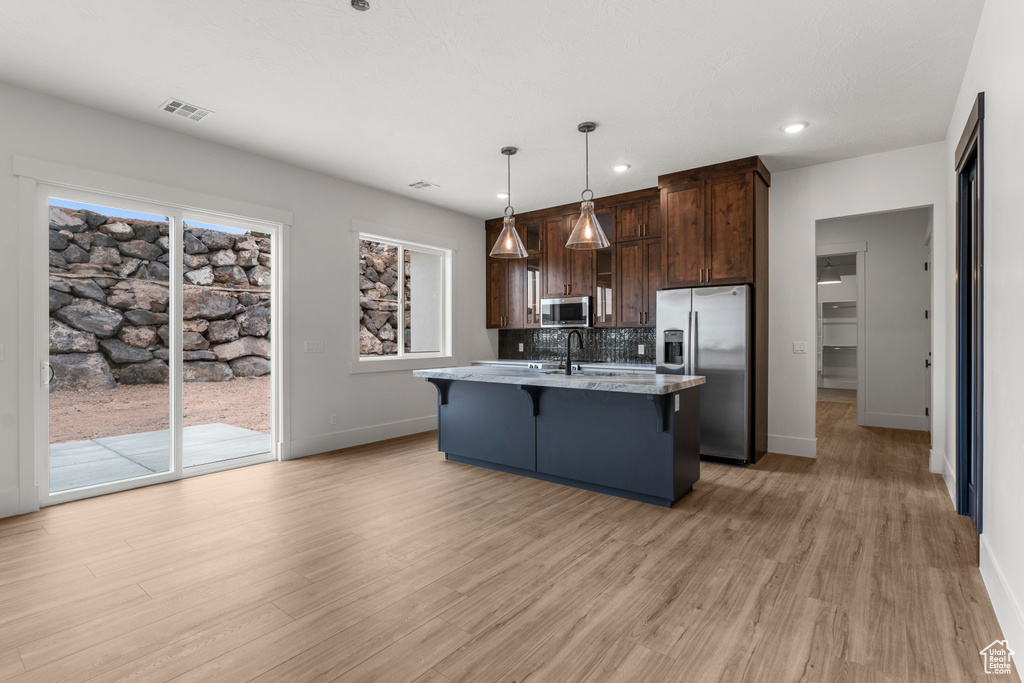 Kitchen with a breakfast bar area, dark brown cabinetry, baseboards, light wood-style floors, and stainless steel appliances