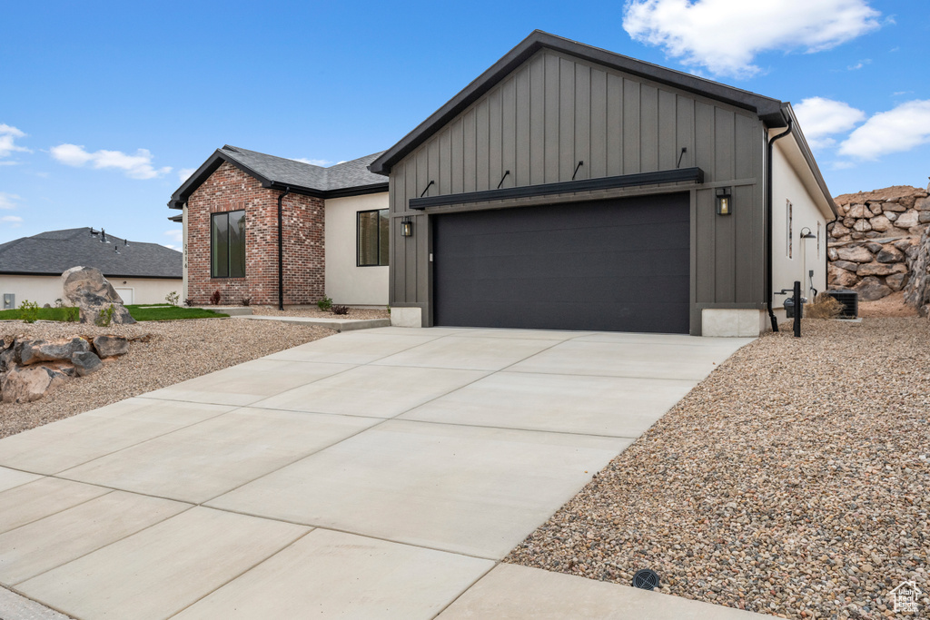 View of front of property featuring board and batten siding, brick siding, an attached garage, and driveway