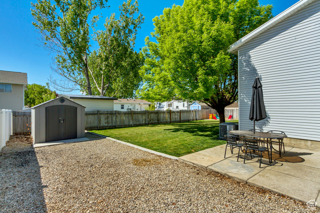 View of yard featuring a storage unit, central AC, a fenced backyard, a patio area, and an outdoor structure