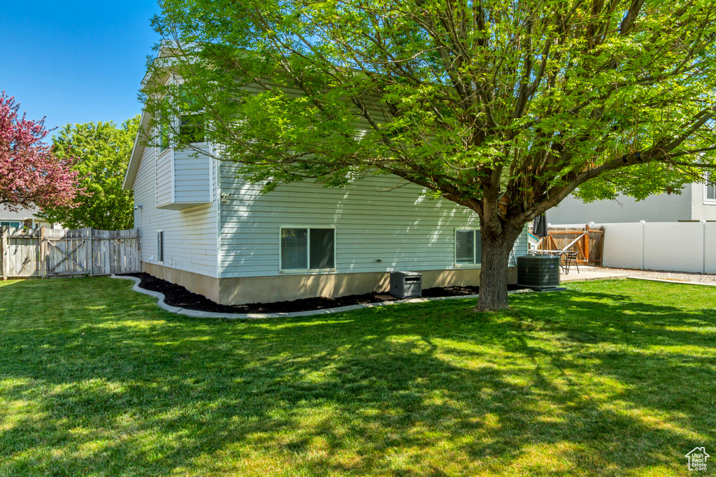 Rear view of house featuring a lawn, central AC, and a fenced backyard