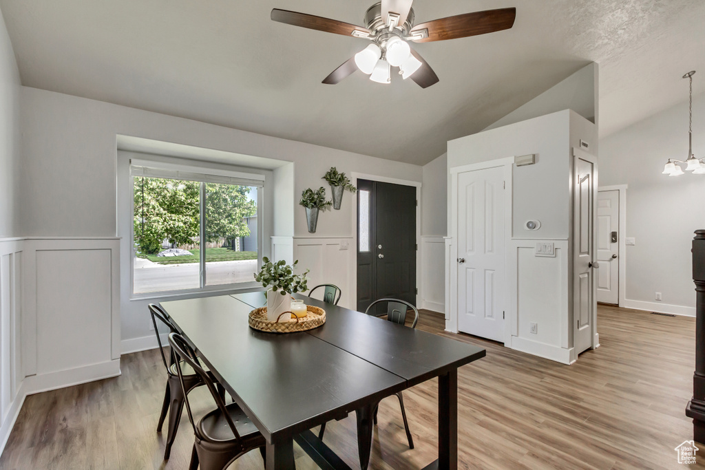 Dining space featuring lofted ceiling, a wainscoted wall, ceiling fan with notable chandelier, and light wood-style floors