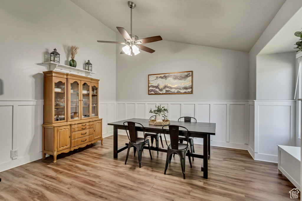 Dining space with wainscoting, a decorative wall, a ceiling fan, lofted ceiling, and light wood-type flooring