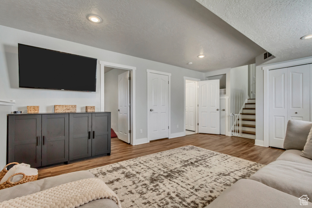 Living room with a textured ceiling, visible vents, baseboards, light wood finished floors, and recessed lighting