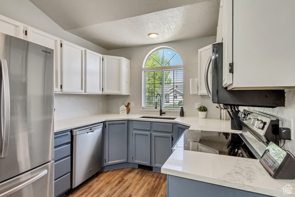 Kitchen featuring appliances with stainless steel finishes, tasteful backsplash, a sink, light wood finished floors, and white cabinetry