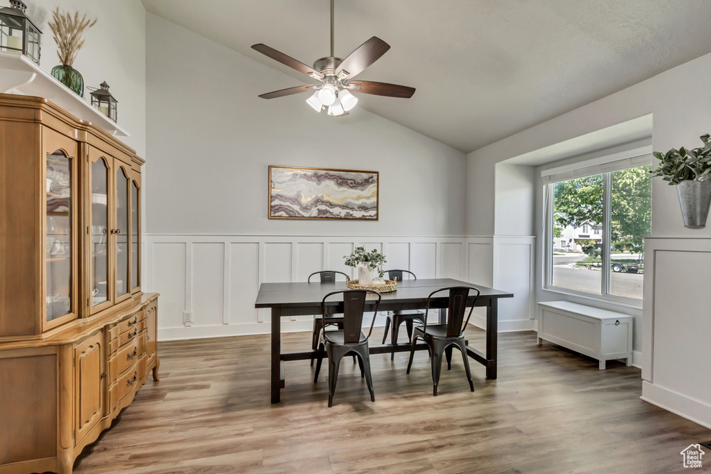 Dining area featuring a decorative wall, ceiling fan, wainscoting, and light wood-type flooring